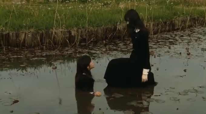 Screen capture from Fatal Frame showing the pond-walking girl kneeling down to another girl who is in the water up to her chest.