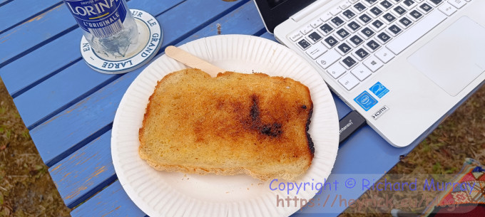 A big piece of buttered bread on a paper plate next to a notebook computer.