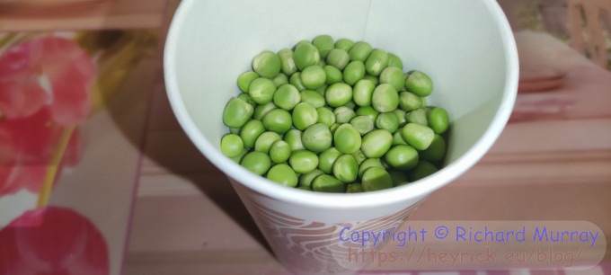 A paper cup with garden peas in it.