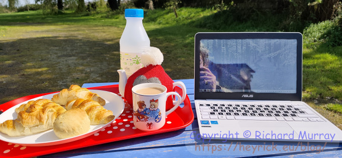Tea and croissants on a picnice table beside a laptop.